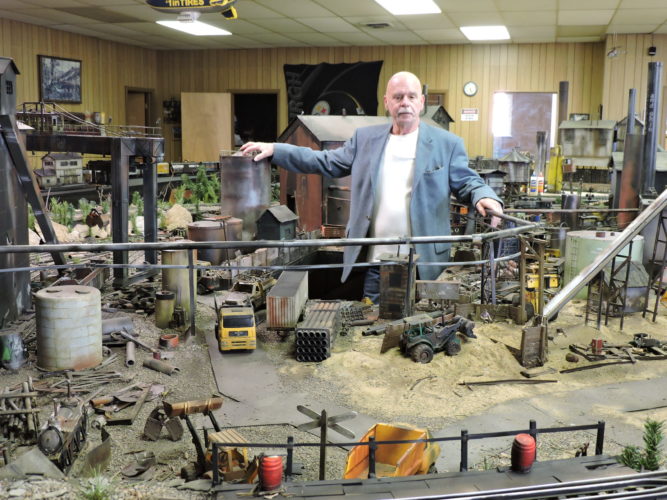 SURVEYING MILL OPERATION -- Larry Caniff stands in a trap door area of his G gauge model train display where he has built a steel mill. Caniff said he used books and photographs to create the mill buildings materials for his train layout. -- Dave Gossett